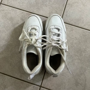 Vita chunky sneakers från NA-KD - Säljer ett par vita chunky sneakers från NA-KD med snörning och tjock sula. Skorna har en sportig look och är tillverkade i syntetmaterial. Perfekta för dig som gillar stilrena och trendiga sneakers. Storlek 38, varsamt använda💗