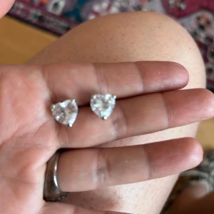 Hjärtformade örhängen i silverfärg - Säljer ett par söta hjärtformade örhängen med gnistrande stenar i silverfärg. Perfekta för att ge en extra touch till din stil. Liknar Caroline Svedbom stil, hämta i Majorna 