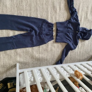 Mörkblå ribbade mjukisbyxor - Mörkblå mjukisbyxor med ribbad struktur och hög midja. Byxorna har en bekväm passform och är perfekta för en avslappnad stil. Matchar med en croppad hoodie i samma färg och material.