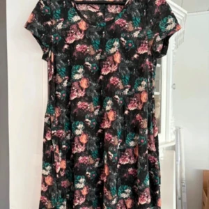 Blommig klänning  - Kortklänning med blommigt mönster i rosa, grönt och svart. Klänningen har korta ärmar och en lös passform, perfekt för en avslappnad stil. Mjukt material som faller fint.