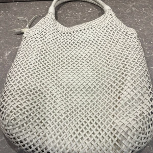 Ljusgrå flätad axelväska - Säljer en vit axelväska från Ceannis. Väskan har snyggt flätat mönster och rundade handtag. Väskan har en mjuk och flexibel form, perfekt för att bära med sig det viktigaste. Enkel och stilren design som passar till många outfits.