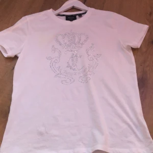 Vit t-shirt med glitter - Vit t-shirt  med ett stort glittrigt emblem framtill, dekorerat med stenar i form av en krona och Klassisk rund halsringning och korta ärmar. Perfekt för dig som gillar lite extra bling i vardagen.har endast använt 3-4 gånger 