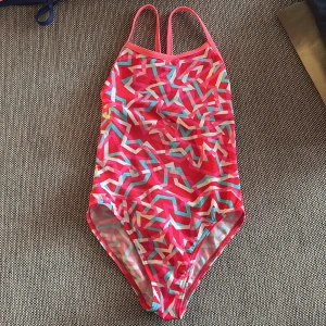 Mönstrad baddräkt från Funkita - Säljer en färgglad baddräkt från Funkita med rosa bas och grafiskt mönster i turkos, vitt och ljusrosa. Modellen har smala axelband och öppen rygg. Perfekt för simträning eller strandhäng. Använd fåtal gånger. Strl: se bild