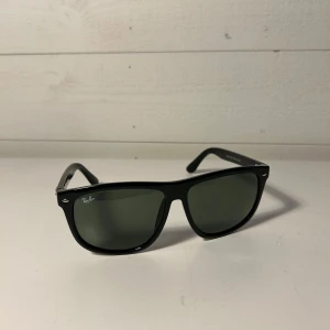 Svarta solglasögon från Ray-Ban - Klassiska svarta solglasögon från Ray-Ban med Wayfarer-inspirerad form. Glasen är mörka och bågarna är i blank svart plast. Perfekta för en stilren look och passar de flesta ansikten.