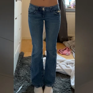 Blå bootcut jeans - Säljer ett par klassiska blå bootcut jeans med låg midja. Jeansen har fem fickor, dragkedja och knapp framtill. Snygg passform som sitter tight upptill och släpper ut vid benen. Perfekta till sneakers eller boots. Gina tricot i storlek 158 men passar mig som är 163