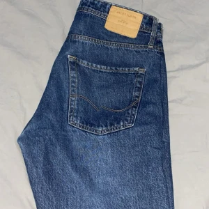 Blå jeansbyxor från Jack&Jones - Klassiska blå jeansbyxor från Jack&Jones med femficksdesign och raka ben. Jeansen har normal passform och är tillverkade i slitstarkt denimtyg. Perfekta för dig som gillar en tidlös och enkel stil.
