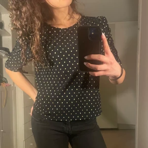 Svart blus med guldprickar - Säljer en svart blus från Holy & White by Lindex med guldprickar. Blusen har trekvartsärm och lätt puff vid axlarna. Perfekt att styla med jeans eller kjol för en snygg look! 