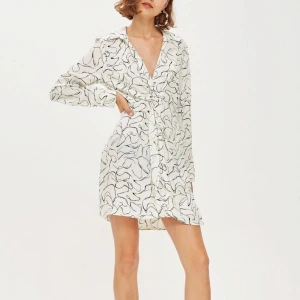 Klänning strl 34, Topshop - Säljer en vit klänning från Topshop med svart abstrakt mönster. Klänningen har lång ärm med knappar på ärmsluten, krage och stängs på sidan. Köpt på Topshop i London men aldrig blivit använd. Material: 100% viskos. Köparen står för frakt. 