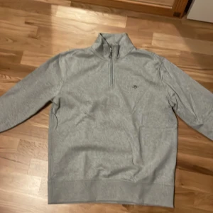 Grå halvzip tröja från GANT - Säljer en stilren grå halvzip tröja från GANT med broderad logga på bröstet. Tröjan är oanvänd fick den för ett tag sen den passade inte och jag gillade den inte. Original pris 1000kr 