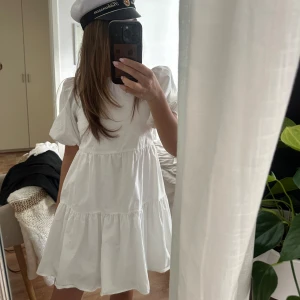 Vit kortklänning med puffärmar och öppen rygg - Säljer en söt vit kortklänning med puffärmar och öppen rygg. Klänningen har en volangig kjol och är perfekt för student eller sommar. Den är tillverkad i ett lätt tyg och har en luftig passform.