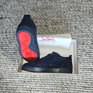 Mörkblå sneakers från Christian Louboutin - Säljer ett par exklusiva mörkblå sneakers från Christian Louboutin med klassisk röd sula och broderad logga på hälen. Skorna har snörning och är tillverkade i mocka med snygga detaljer. Perfekta för dig som vill sticka ut med stil. Storlek 44, Box, Äktheten verifikations kort, dustbag, Care instructions och övriga lappar medföljer. Helt oanvända. Nypris ca 11800kr, mitt pris 2499kr. Priset är inte hugget i sten. Jag fick dessa i födelsedagspresent från min farmor och har köpbevis.