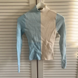 Ribbad tvåfärgad polotröja från & Other Stories - Säljer en ribbad polotröja från & Other Stories i färgblock med ljusblått och vitt. Tröjan har lång ärm och tight passform, perfekt för att lyfta din outfit med en cool touch.