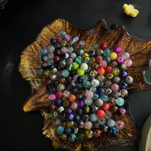 Färgglada pärlor i glas - Säljer ett mixat set med färgglada glaspärlor i olika former och mönster. Perfekta för att skapa egna smycken som armband, halsband eller örhängen. Pärlorna kommer i en dekorativ skål i form av ett löv.