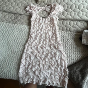 Ljusrosa volangklänning med öppen rygg - Supersöt ljusrosa klänning med volangdetaljer över hela och en snygg öppen rygg med rosett. .