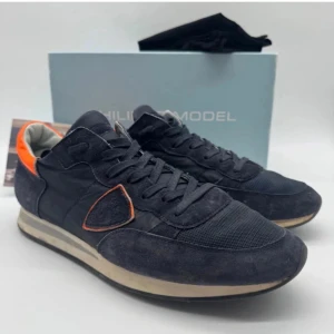 Svarta sneakers från Philippe Model - Snygga svarta sneakers från Philippe Model med orange detaljer. Skorna har en klassisk design med snörning och en bekväm sula. Perfekta för en stilren look.