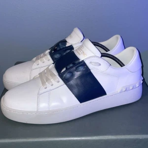 Valentino Open sneakers i vitt och marinblått - Säljer ett par snygga Valentino Open sneakers i vitt skinn med bred marinblå rem över mitten. Klassisk rund tå och platt sula. Perfekta för dig som gillar stilrena och exklusiva sneakers.