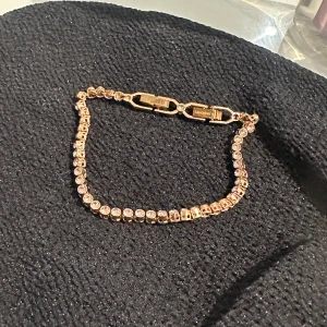 Guldfärgat armband med kristaller från Swarovski - Elegant armband i guldfärg från Swarovski, dekorerat med gnistrande runda kristaller längs hela bandet. Klassisk och stilren design med säker låsning, perfekt för att ge en lyxig touch till din outfit.