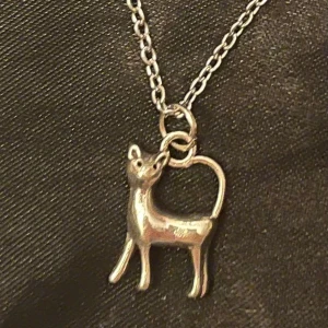 Katt halsband silver imitation  - Fint halsband med en berlock i form av en liten silvrig katt. Berlocken är ca 1,5 x 0,8 cm. Trädd på kedja i silverimitation som är justerbar 40-45 cm. 