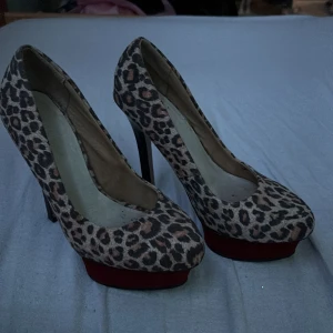 Leopardmönstrade pumps från Bianco - Snygga pumps från Bianco med leopardmönster och röd platåsula. Skorna har hög klack och rund tå, samt svart detalj vid hälen. Materialet är mockaliknande och ger en lyxig känsla. Perfekta för dig som vill sticka ut med djurmönster och höjd.