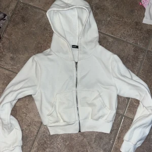 Vit croppad hoodie från SHEIN - Snygg vit croppad hoodie från SHEIN med dragkedja framtill och två stora fickor. Mjuk fleece på insidan och huva för extra cozy känsla. Perfekt till jeans eller mjukisbyxor när du vill ha en chill look.