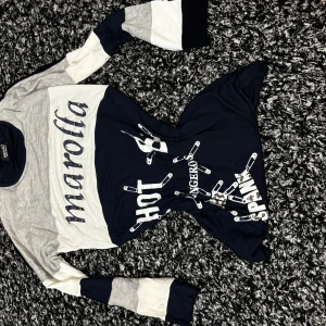 Randig långärmad tröja med tryck från Maroffa - Säljer en långärmad tröja från Maroffa i blått, grått och vitt med tryck av säkerhetsnålar och texten 'HOT', 'SPANK', 'DANGEROUS'. Tröjan har blockfärgade ärmar och en cool streetstil.2000s vibe 