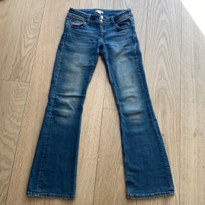 Blå bootcut jeans med dubbla knappar - Snygga blå jeans från Gina  Tricot med bootcut passform och dubbla knappar i midjan. Jeansen har klassiska fickor fram och bak, samt lätt slitna detaljer på låren. 