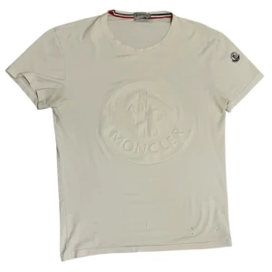 Vit t-shirt från Moncler - Säljer min gamla moncler t shirt eftersom att den blivit för liten för mig. Finns några defekter så som en fläck och två små hål på framsidan och på baksidan som är inte märkligt om man inte kollar nogrant. Skick 6.5/10, storlek xs. Hör av er vid minsta fundering