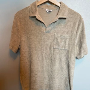 Beige frotté pikétröja från East West - Säljer en beige pikétröja i mjuk frotté från East West. Tröjan har korta ärmar, klassisk krage och en bröstficka. Perfekt för chill vår- och sommardagar. Enkel och stilren design som är lätt att matcha.