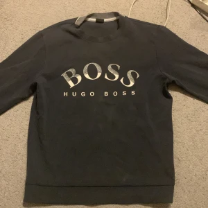 Mörkblå sweatshirt från Hugo Boss - Snygg mörkblå sweatshirt från Hugo Boss med stor silverfärgad BOSS-logga framtill. Klassisk rund halsringning och långa ärmar. Perfekt för en stilren och enkel look.