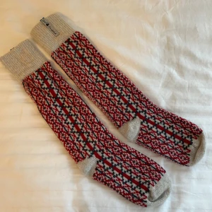 Mönstrade ullstrumpor från Öjbro vantfabrik - Långa stickade ullstrumpor med klassiskt rutig mönster i rött, blått och beige. Ribbstickad beige mudd och tå, perfekt för kalla dagar. Snygg retrostil och svensk design. Helt oanvänfa. Storlek 36-38