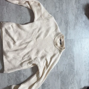 Beige ribbad stickad tröja H&M - Säljer en beige stickad tröja från H&M med ribbad struktur och hög hals. Tröjan har långa ärmar och en relaxed passform, perfekt för lager-på-lager. Enkel och stilren design som funkar till många outfits.