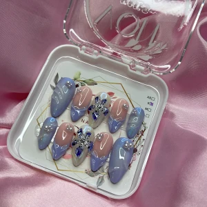 Iris (S);Medium Almond - Snygga gelé-press-on naglar i medium mandelform med ljusblå och nude färg, dekorerade med pärlor och glittriga detaljer. Två naglar har 3D-blommor. Kommer i storlek S: 15 mm, 11,5 mm, 12 mm, 11 mm, 9 mm. Perfekt för dig som vill ha unika och trendiga naglar.