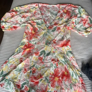 Blommig kortklänning från H&M - Superfin kortklänning från H&M med färgglatt blommönster i rött, gult och grönt på vit botten. Klänningen har v-ringning, puffiga korta ärmar och lätt utställd kjol. Perfekt för sommarens alla tillfällen!