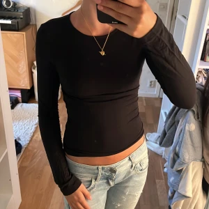 Svart croppad långärmad topp - Säljer en svart, tight och croppad långärmad topp med rund halsringning. Perfekt att matcha med jeans eller kjol för en stilren look. Enkel och stilren design utan synliga detaljer eller mönster.