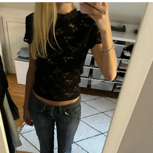 Svart spetsblus från Zara - Säljer en svart, genombruten spetsblus från Zara med korta ärmar och hög hals. Blusen har ett elegant blommönster och är figurnära i modellen. Perfekt att styla till både jeans och kjol!