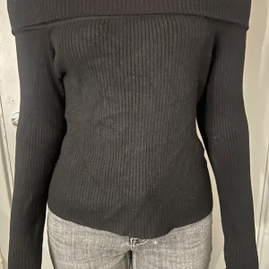 Svart ribbad offshoulder-tröja - Säljer en svart ribbad offshoulder-tröja med lång ärm. Tröjan har en tight passform och bred kant upptill som sitter snyggt över axlarna. Perfekt för dig som vill ha en stilren och trendig look.