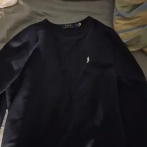 Mörkblå tröja från Polo Ralph Lauren - Säljer en klassisk mörkblå tröja från Polo Ralph Lauren med rund halsringning och den ikoniska broderade loggan på bröstet. Perfekt för en stilren och enkel look.