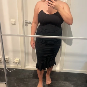 Svart tight klänning med volangkant - Säljer en svart tight klänning med volangdetalj nertill. Klänningen har figurnära passform och rynkade partier längs sidorna som ger en snygg siluett. Perfekt för dig som vill ha en stilren och elegant look.