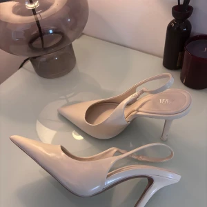 Vita pumps med klack från Zara - Säljer ett par stilrena vita pumps från Zara med spetsig tå och öppen häl. Skorna har en elegant klack och smal rem runt hälen. Perfekta för dig som gillar en klassisk och trendig look.
