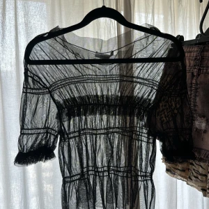 Svart mesh blus  - Säljer en svart transparent blus med puffiga korta ärmar och resårdetaljer. Perfekt för att styla lager på lager eller över ett linne. Tunn och luftig modell med fina sömdetaljer.
