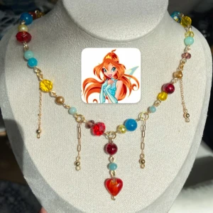 Färgglatt halsband med hjärthänge - Unikt halsband med pärlor i rött, blått, gult och guld på guldfärgad kedja. Dekorativa kedjor hänger ner och i mitten finns ett rött hjärthänge. Perfekt statement-piece för dig som gillar färg och lekfull stil. Inspirerat av karaktären Bloom i tv-serien Winxclub. 