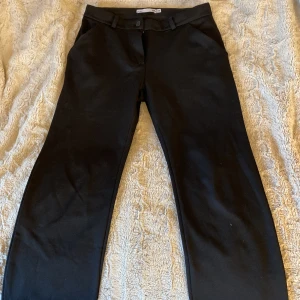 Svarta kostymbyxor från 157 - Svarta kostymbyxor från 157 med klassisk rak passform och bälteshällor. Byxorna har knapp och dragkedja framtill samt sidfickor. Perfekta för en clean och stilren look. Materialet känns som bomullsmix.