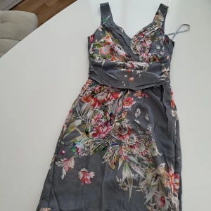 Blommig grå kortklänning från s.Oliver i Siden. - Supersnygg kortklänning från s.Oliver Selection i grått med färgglatt blommönster. Omlott upptill, breda axelband och markerad midja. 100% siden. Lätt och flowy känsla, perfekt för sommarens alla tillfällen. 