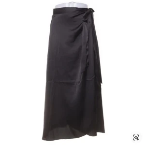 Svart omlottkjol i satin - Snygg svart omlottkjol i satin med knytband i midjan. Kjolen har en lång och elegant siluett som ger en stilren look. Perfekt att styla med en enkel topp eller stickad tröja.