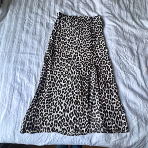 Leopardmönstrad långkjol från H&M - Snygg långkjol från H&M med leopardmönster i beige, svart och bruna toner. Kjolen har en rak och flowy passform som ger en chill vibe. Perfekt för dig som vill sticka ut med ett djurmönster och skapa en trendig look.