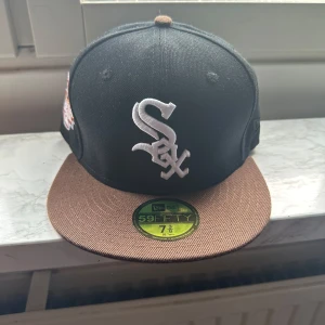 Chicago White Sox 59FIFTY fitted keps 7 3/8, 58,7 cm - Snygg 59FIFTY keps från New Era med Chicago White Sox-logga framtill och 2003 All Star Game patch på sidan. Kepsen är svart med brun skärm och har broderade detaljer i vitt och brunt. Klassisk flat brim och MLB-logga bak. Perfekt för dig som gillar sportig streetstyle.