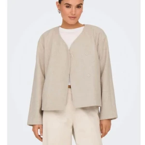 Beige kappa från ONLY - Stilren beige kappa med minimalistisk design och v-ringad halsringning. Jackan har lång ärm och knäpps framtill med dolda knappar. Tillverkad i ett mjukt material som ger en avslappnad men ändå snygg look. Storlek s och aldrig använd.