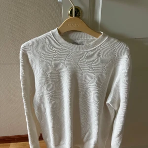Vit stickad tröja från These Glory Days - Säljer en vit stickad tröja från These Glory Days med snyggt vågigt strukturmönster. Tröjan har rund halsringning och långa ärmar, perfekt för lager på lager. Enkel att matcha med jeans eller kjol för en clean look.