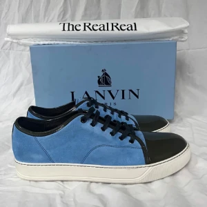 Exklusiva lanvins skor - Snygga sneakers från Lanvin i blå mocka med svart lackad tå och svarta snören. Skorna har vit platt sula och rund tå, vilket ger en clean och modern vibe. Perfekta för dig som vill sticka ut med stilrena detaljer och lyxig känsla.