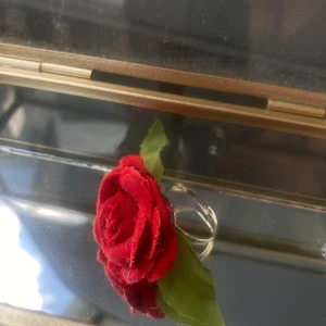 Handgjord ring med röd tygros - Cool ring med en röd tygros och gröna blad på en justerbar silvrig ringbas. Perfekt för dig som vill sticka ut och addera en romantisk touch till din stil. Ringen har en tydlig blommig vibe och är iögonfallande på bästa sätt!